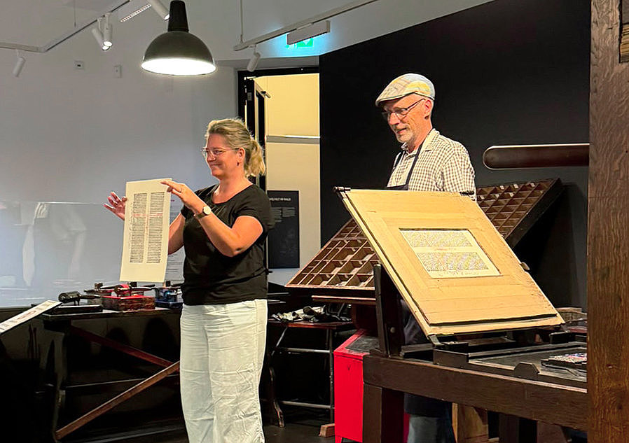 Referendarin zeigt einen frisch erstellten Druck einer historischen Druckerpresse