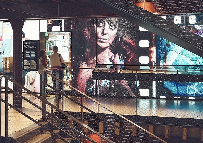 Blick durch das Treppenhaus des Nederlands Fotomuseum auf ein großformatiges Frauenporträt mit sichtbarer Filmperforation.