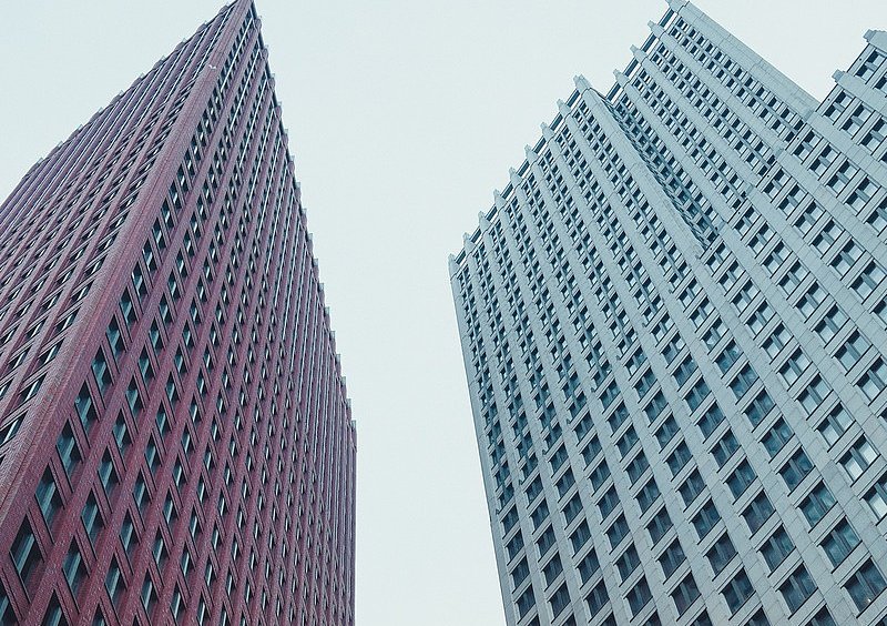 Blick steil nach oben zwischen einem roten und einem hellgrauen Hochhaus in Den Haag.