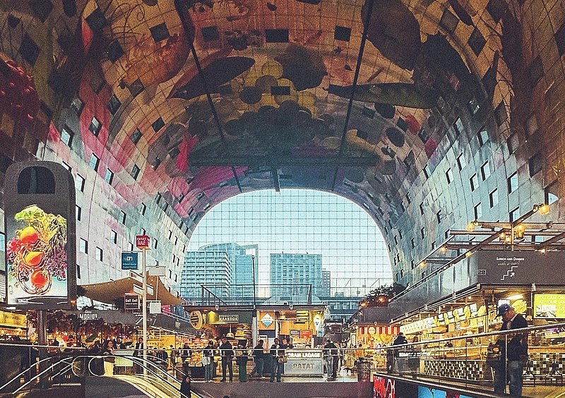  Innenraum der Rotterdamer Markthal mit beleuchteten Verkaufsständen und einem farbenfrohen Deckenbild aus Früchten und Pflanzen.
