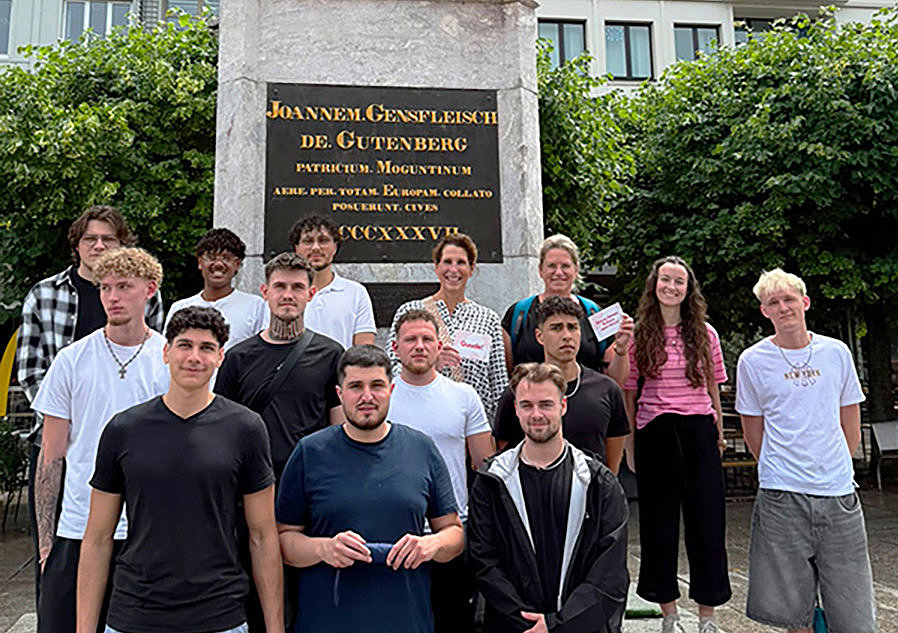 Gruppenfoto von Auszubildenden der Maschinen- und Anlagenführung sowie Lehrkräften vor dem Gutenberg-Denkmal in Mainz
