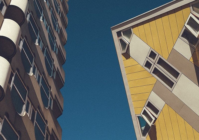 Blick nach oben zwischen einem gelben Kubushaus und einem benachbarten Hochhaus in Rotterdam.
